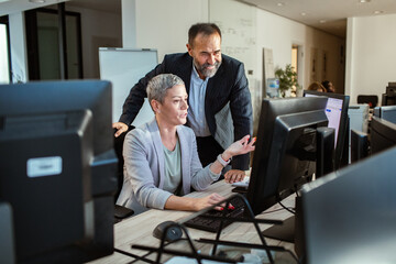 Team collaboration at office desk with dual monitors and brainstorming