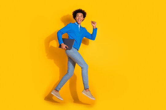 Full body photo of attractive young man hold netbook running dressed stylish blue clothes isolated on yellow color background