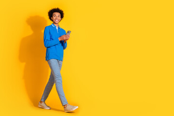 Full body portrait of nice young man hold phone walk empy space isolated on yellow color background © deagreez