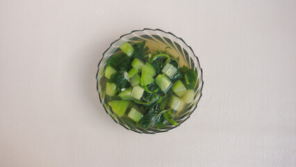 A bowl of soup with green vegetables in it. 