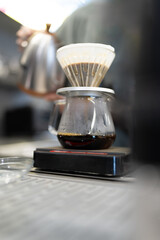 Professional barista making filtered drip coffee in coffee shop. Close up of hands barista brewing a drip hot espresso coffee, pour over coffee with hot water and filter paper in coffee cafe.