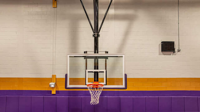 New ceiling mounted basketball hoop with clear glass, acrylic backboard, in a indoor school gym.
