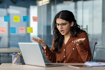 A businesswoman faces a challenge using her laptop in an office, expressing confusion and...