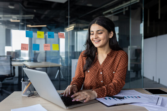 Young professional woman typing on a laptop, analyzing data charts, and brainstorming ideas in an office.