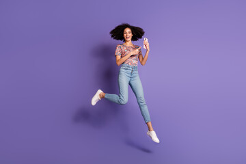 Energetic young woman with curly hair jumps joyfully while pointing at a phone, set against a...