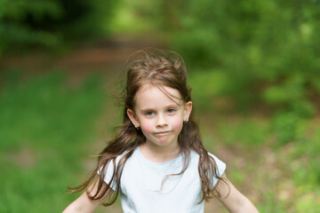 Sad girl in a T-shirt and denim shorts on a dirt path in a summer forest. Concept of a tired healthy active child