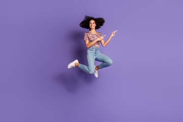 A young woman with beautiful curls jumps joyfully against a vibrant purple backdrop, exuding...