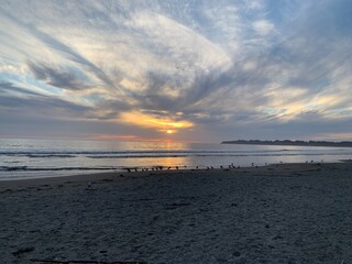This beautiful beach scene captures the sun setting over the horizon, casting a warm golden glow on the ocean.