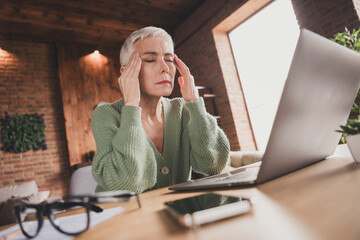 Obraz premium Elegant mature woman experiencing a moment of stress while working at home