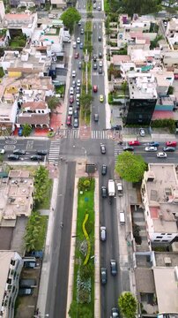 Trafico de carros y gente caminando por la acera en un cruce de una avenida llena de arboles y rodeada de edificios y casas vista desde un drone