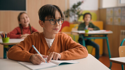 Caucasian little boy kid schoolboy nerd in glasses write task class lesson school education angry...