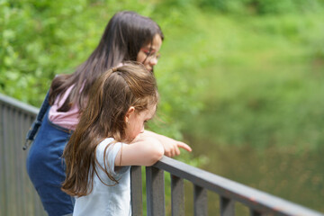 Two cute little girls hang on the railings in the park summer pond. Concept of active childhood outdoors