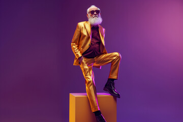 Obraz premium An elderly man in a metallic gold suit strikes a pose against a vibrant purple backdrop. Bold contemporary fashion and confidence.