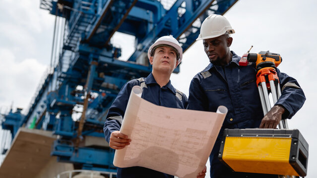 The survey team is using a theodolite and road construction plans to take measurements. Civil engineers are working with surveying tools to collect data for the construction project.