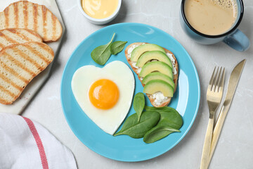 Romantic breakfast with heart shaped fried egg served on light grey table, flat lay