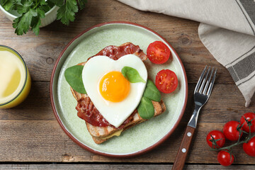 Tasty sandwich with heart shaped fried egg and bacon on wooden table, flat lay