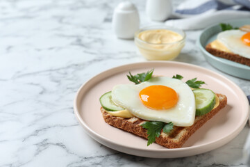 Plate of tasty sandwich with heart shaped fried egg on white marble table