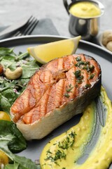 Tasty grilled salmon steak with sauce and salad on table, closeup