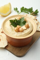 Delicious hummus with parsley, chickpeas, pita and lemon on white table, closeup