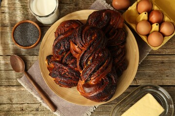 Tasty buns with poppy seeds and ingredients on wooden table, flat lay