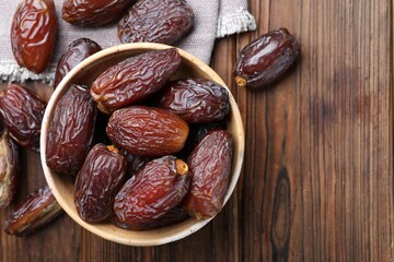 Many tasty dried dates in bowl on wooden table, top view. Space for text