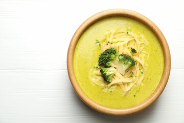 Delicious broccoli cream soup in bowl on white wooden table, top view. Space for text