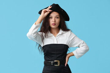 Beautiful young Asian woman dressed as pirate on blue background
