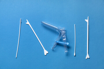 Gynecological speculum with pap smear test tools on blue background, top view