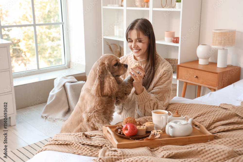 Wall mural Beautiful young happy woman and cute Cocker Spaniel dog with cup of green tea eating muffins at home