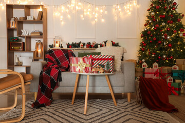 Table with gift boxes, decor and beautiful Christmas tree in interior of modern living room