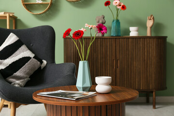 Beautiful gerberas in vase and magazine on table in interior of living room