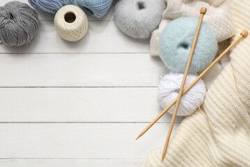 Colorful knitting yarn with needles and sweater on white wooden background