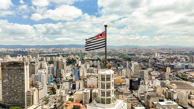 Foto a&eacute;rea da bandeira da cidade de S&atilde;o Paulo no topo do Farol Santander, destacando o skyline da cidade ao fundo. Foto feita em S&atilde;o Paulo, SP em 12 dez 2024