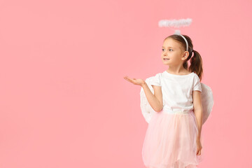 Cute little girl dressed as Cupid pointing at something on pink background. Valentine's Day...