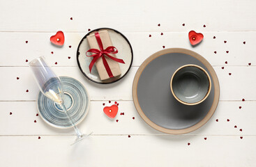 Beautiful table setting with gift box and burning candles on white wooden background. Valentine's Day celebration