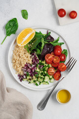 Quinoa salad with tomatoes, lettuce leaves, cucumber, onion in plate on white background with copy space