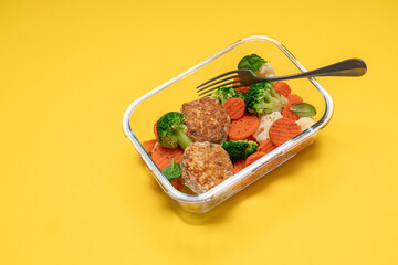 Broccoli, carrot, cauliflower and chicken breast cutlets. Healthy food in glass container on yellow background