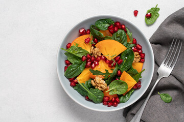 Persimmon salad with pomegranate seeds, spinach and walnuts in bowl on white background with copy space. New Year and Christmas menu