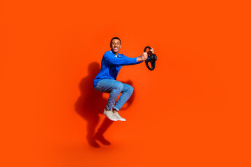 Happy young man in blue shirt posing joyfully against vibrant orange backdrop
