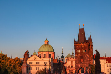Fototapeta premium Sunset view from iconic Charles Bridge in Old Town Prague, Czechia. Gothic Old Town Bridge Tower with golden hour light. Baroque dome of the Church of St. Francis of Assisi in background. Tourism