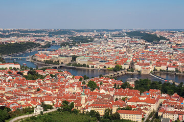 Obraz premium Aerial view of Prague seen from Petrin tower, Czechia. City's iconic landmark Charles Bridge is visible in distance. Vltava River winds through city. Historic city center with its red-tiled roofs