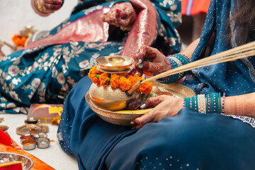 A traditional Indian woman holds a pooja plate and applies kumkum on a decorated brass Karwa for the Karwa Chauth pooja, which is an Indian tradition.
