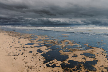 The sea and the beach are polluted with fuel oil. Beach oil spill impact, pollution, waste disposal. Ecology catastrophe.