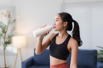 Young asian sportswoman drinking milk from bottle after workout at home, healthy lifestyle concept