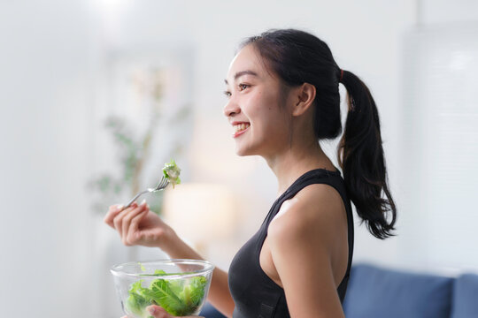 Happy asian woman enjoying a fresh salad after completing a workout at home, embracing a healthy lifestyle and nourishing her body