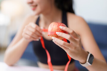 Woman holding and measuring a red apple with a red measuring tape, promoting healthy eating habits...