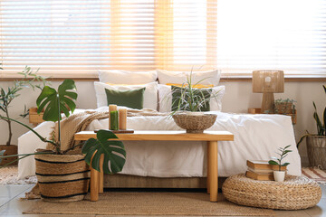 Interior of light bedroom with green plants, bench and window