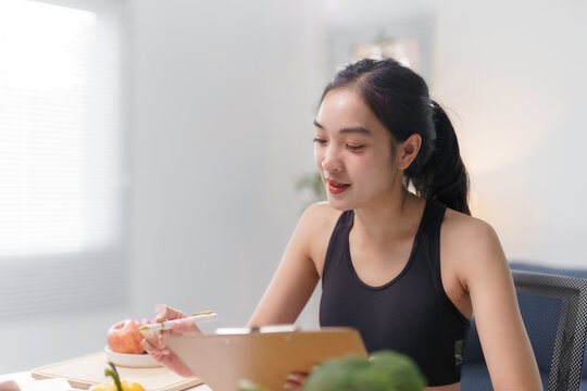 Young woman in athletic wear writing on a clipboard, discussing fitness plans in a bright indoor space, promoting healthy lifestyle concepts