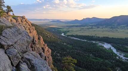 Obraz premium Scenic sunset view from a rocky cliff overlooking a vast valley, river, and distant mountains.