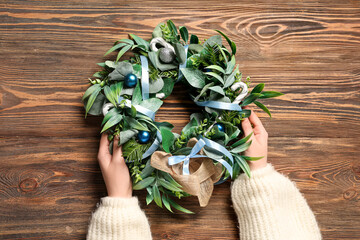 Female hands with beautiful mistletoe wreath on brown wooden background